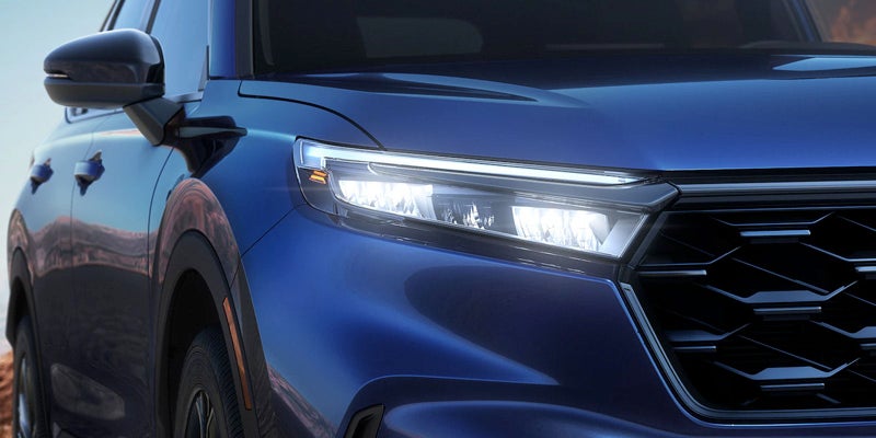 Close-up of a blue car's front right section, showing the illuminated LED headlight and part of the black grille.